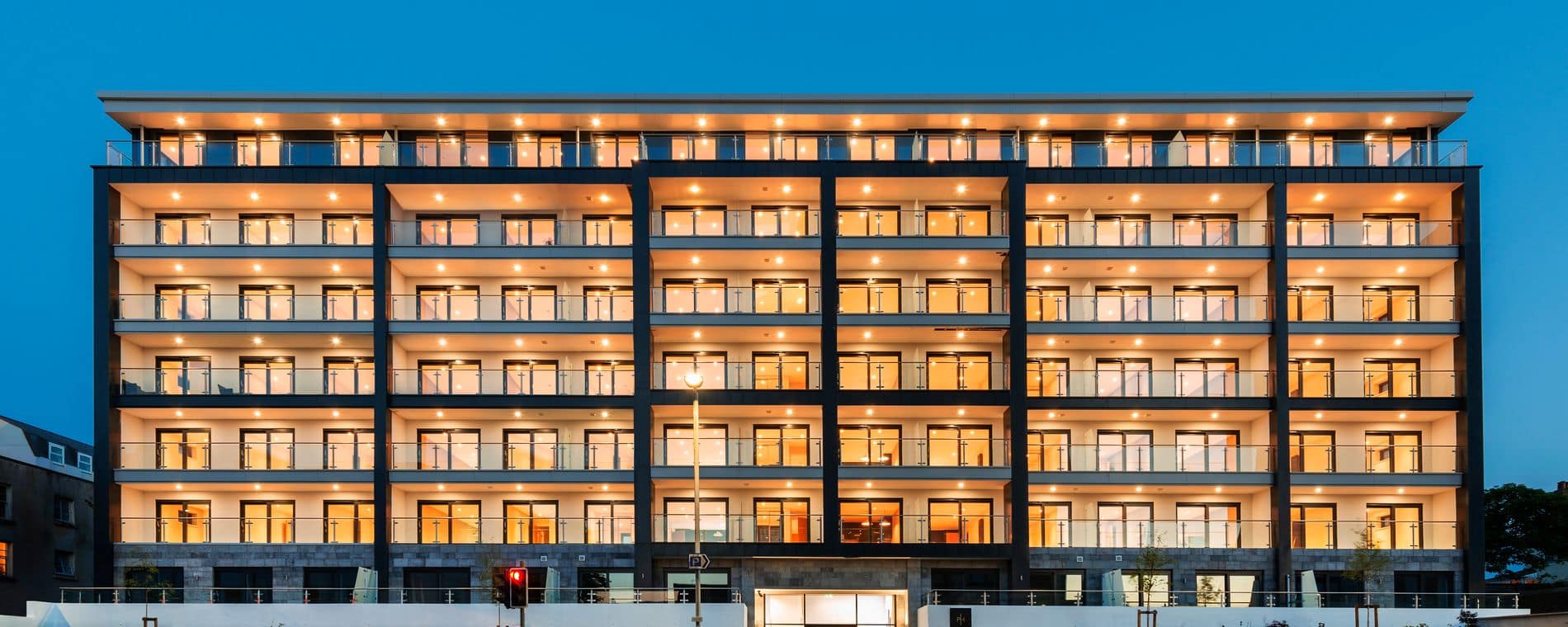 A city-centre apartment building at dusk, windows and balconies lit.